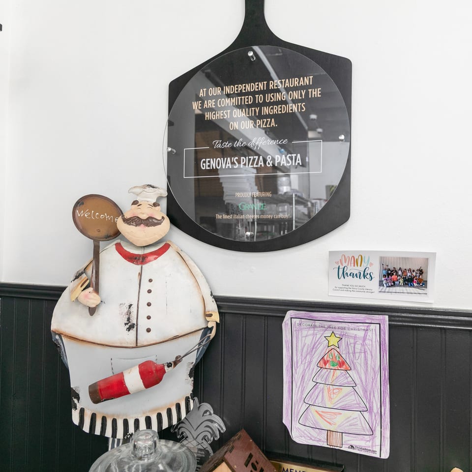 A chef figurine, a Genova's Pizza & Pasta sign, and children's artwork adorn a white wall.