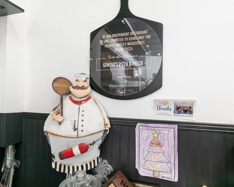 A chef figurine, a Genova's Pizza & Pasta sign, and children's artwork adorn a white wall.