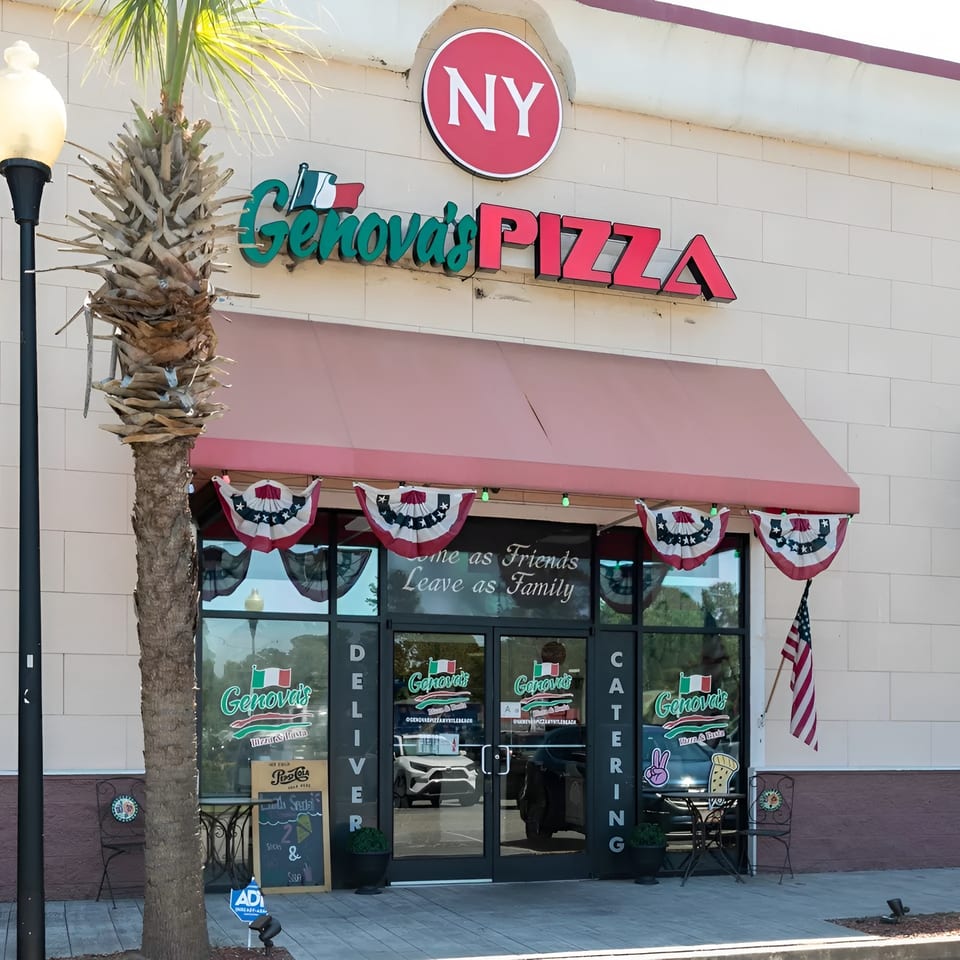 The exterior of Genova's Pizza restaurant with a red awning and patriotic bunting.