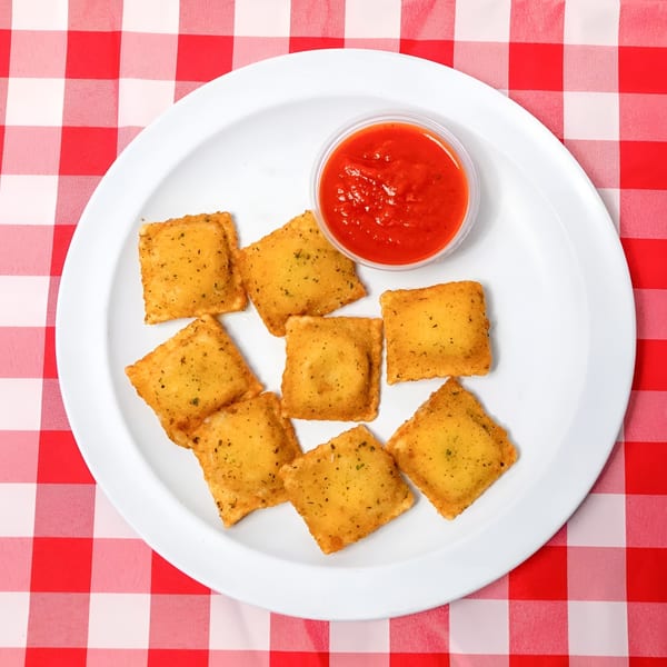 Golden fried ravioli with a side of red marinara sauce on a white plate over a red and white checkered tablecloth.