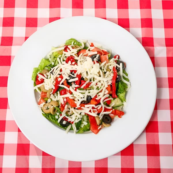 A fresh garden salad with lettuce, tomatoes, olives, red peppers, and shredded cheese on a red and white checkered tablecloth.