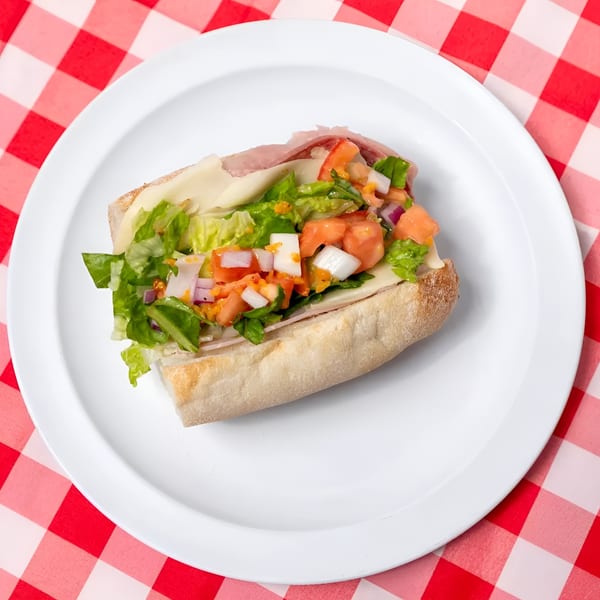 A fresh Italian sub sandwich with lettuce, tomato, onion, and deli meats on a white plate.