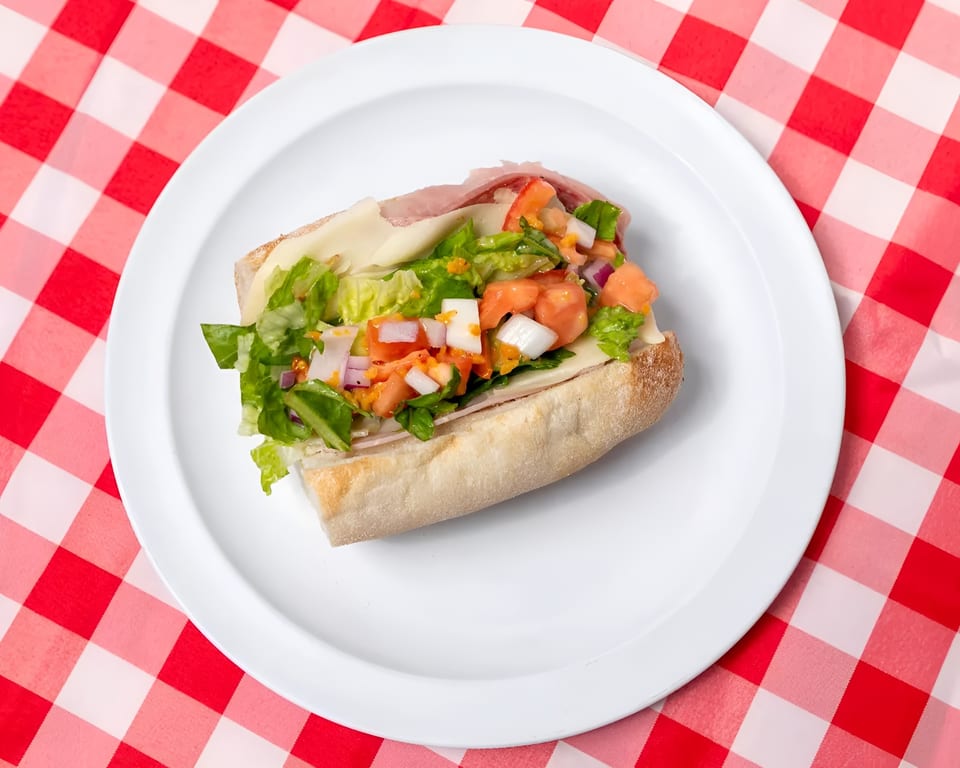 A fresh Italian sub sandwich with lettuce, tomato, onion, and deli meats on a white plate.