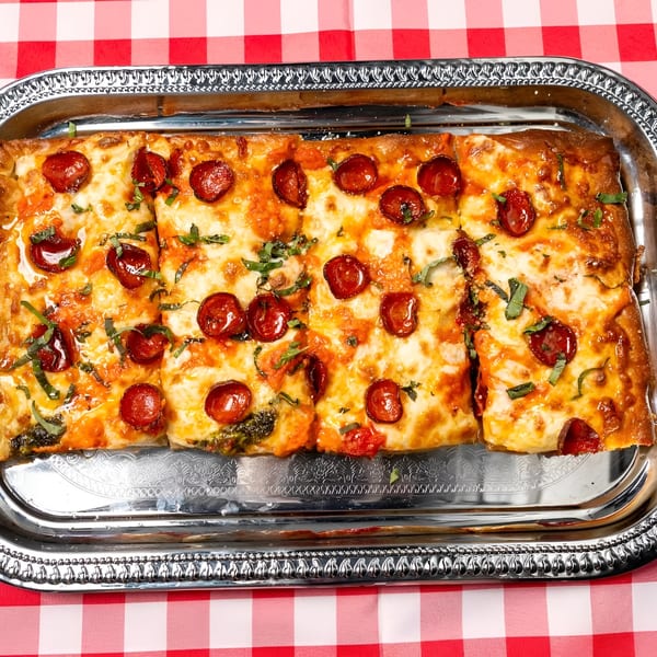 Rectangular pepperoni pizza with basil on a silver tray, on a red and white checkered tablecloth.