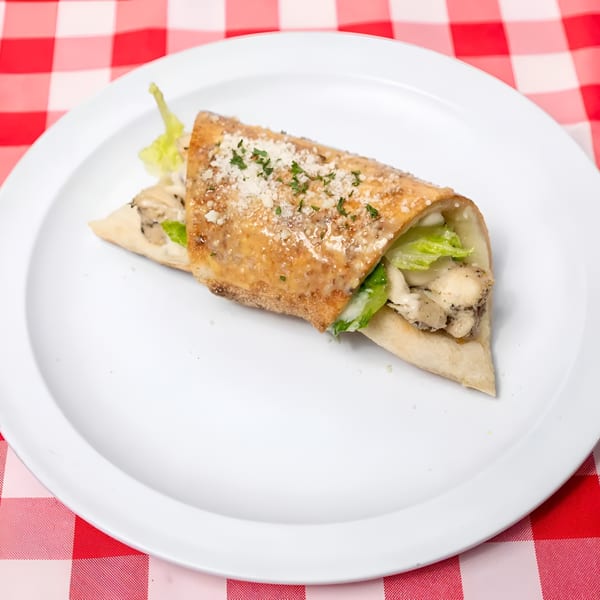 Chicken Caesar wrap with lettuce, parmesan, and dressing on a white plate over a red and white checkered tablecloth.